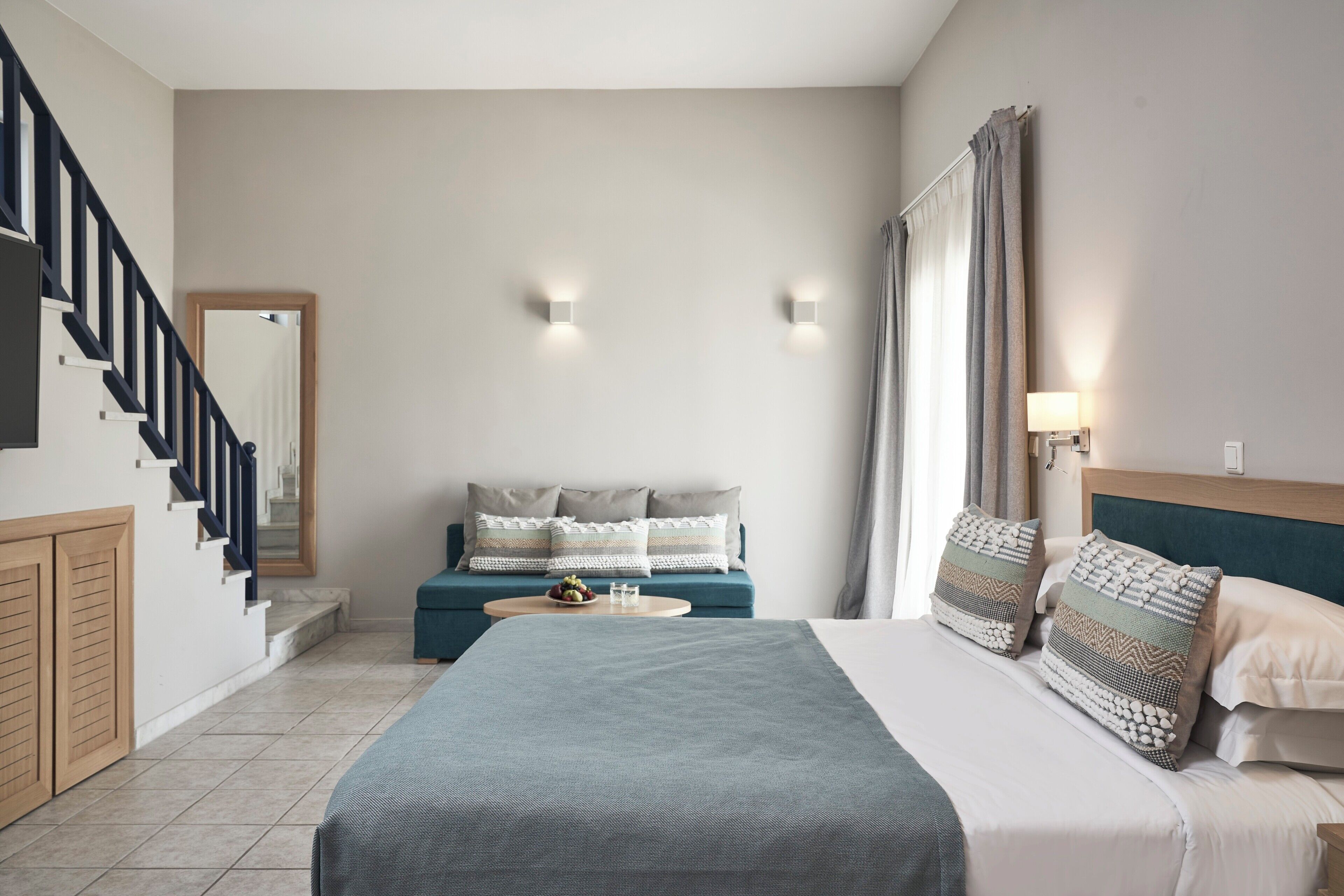 A bedroom with a bed, a sofa, a staircase, and a view of the outside.