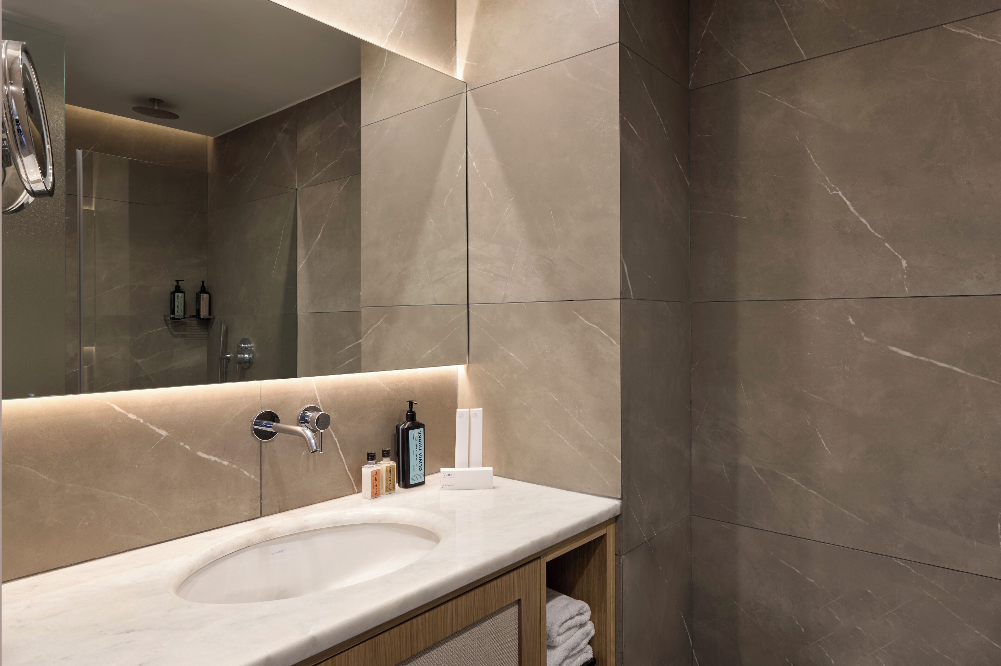 A modern bathroom with a large mirror, a sink, and a vanity with toiletries.