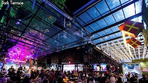 A crowded indoor venue with a glass ceiling, tables, chairs, and a stage for performances. - The Park Residence at Bangkok (Bangkok)
