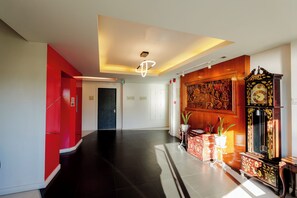 A hotel lobby with a black floor, red walls, a wooden panel wall with a clock, and a ceiling light fixture.