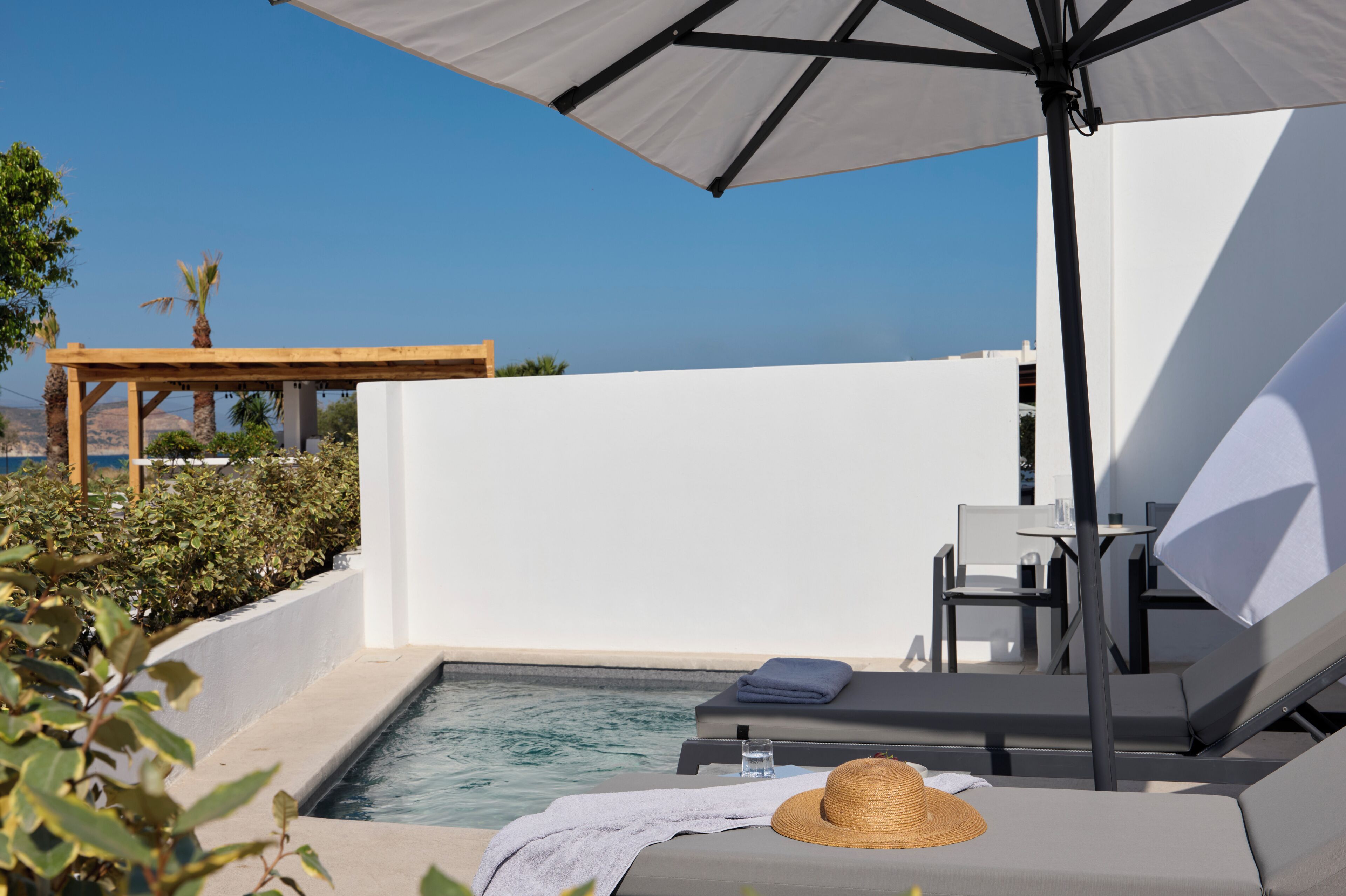 Zona junto a la piscina con una silla de descanso, una mesa y una sombrilla.