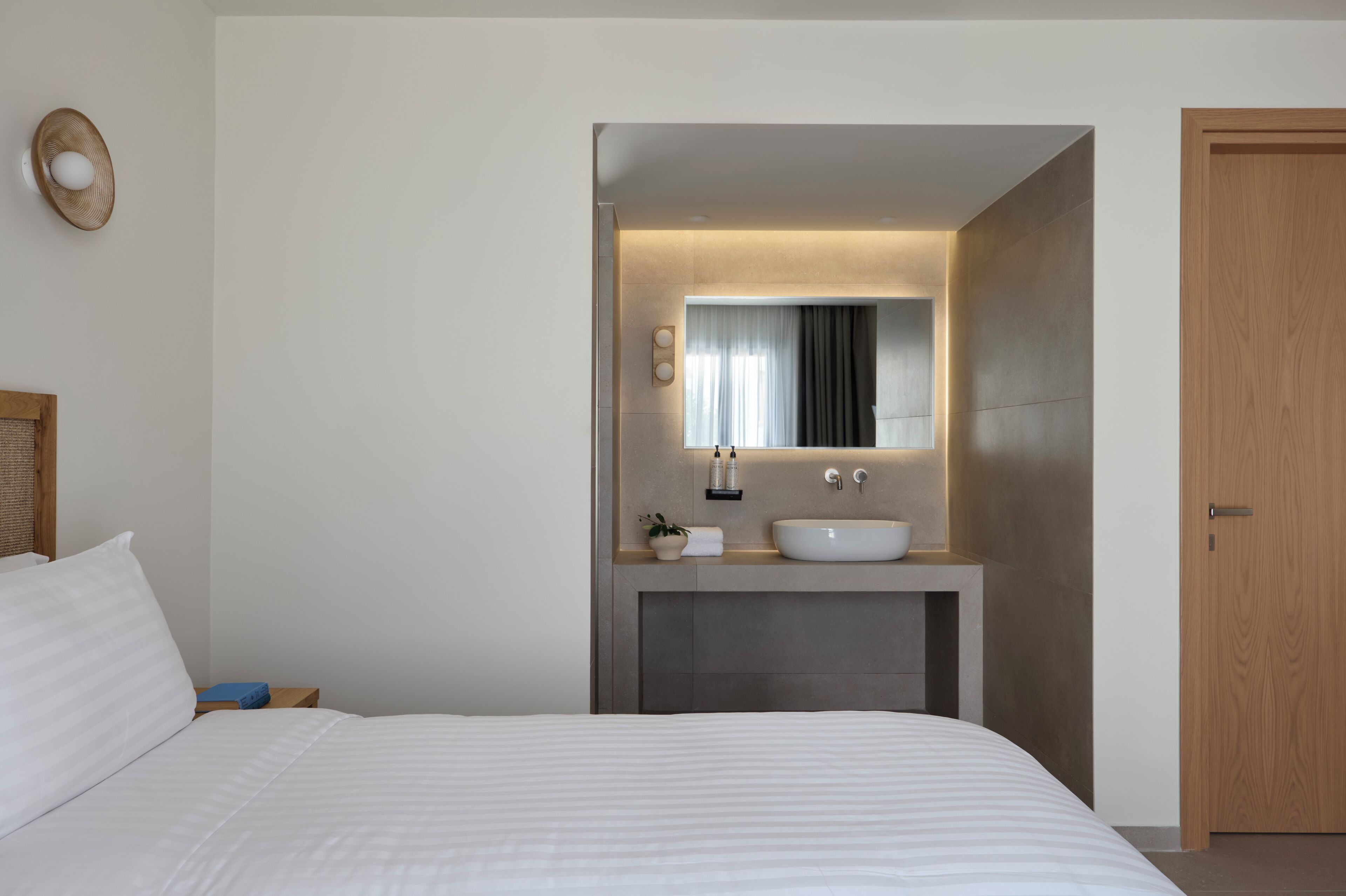 Une chambre à coucher moderne avec un grand lit, une coiffeuse intégrée avec un miroir et une porte en bois.