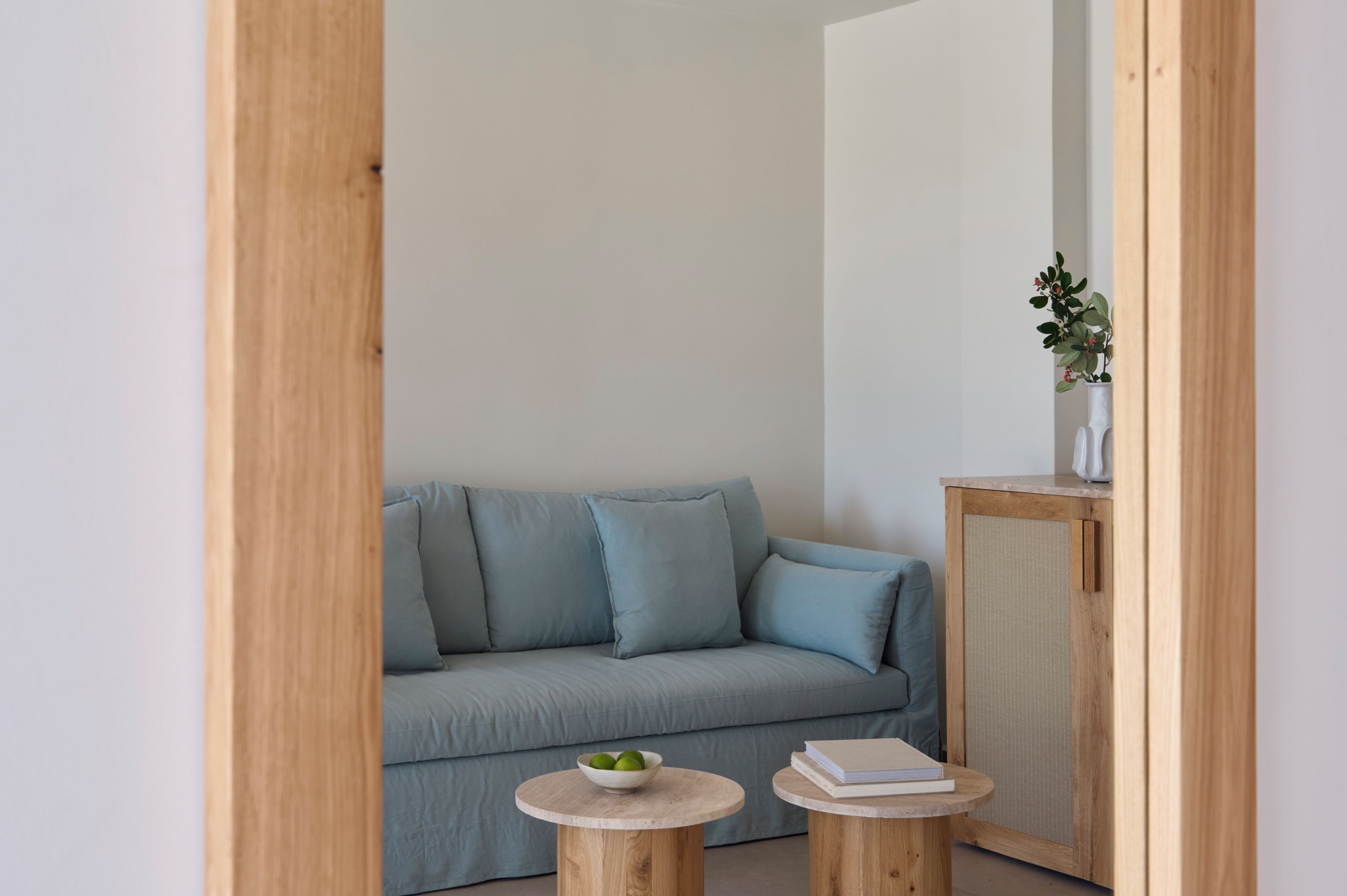 Una habitación con un sofá azul claro, dos mesas redondas de madera y un aparador con una planta.