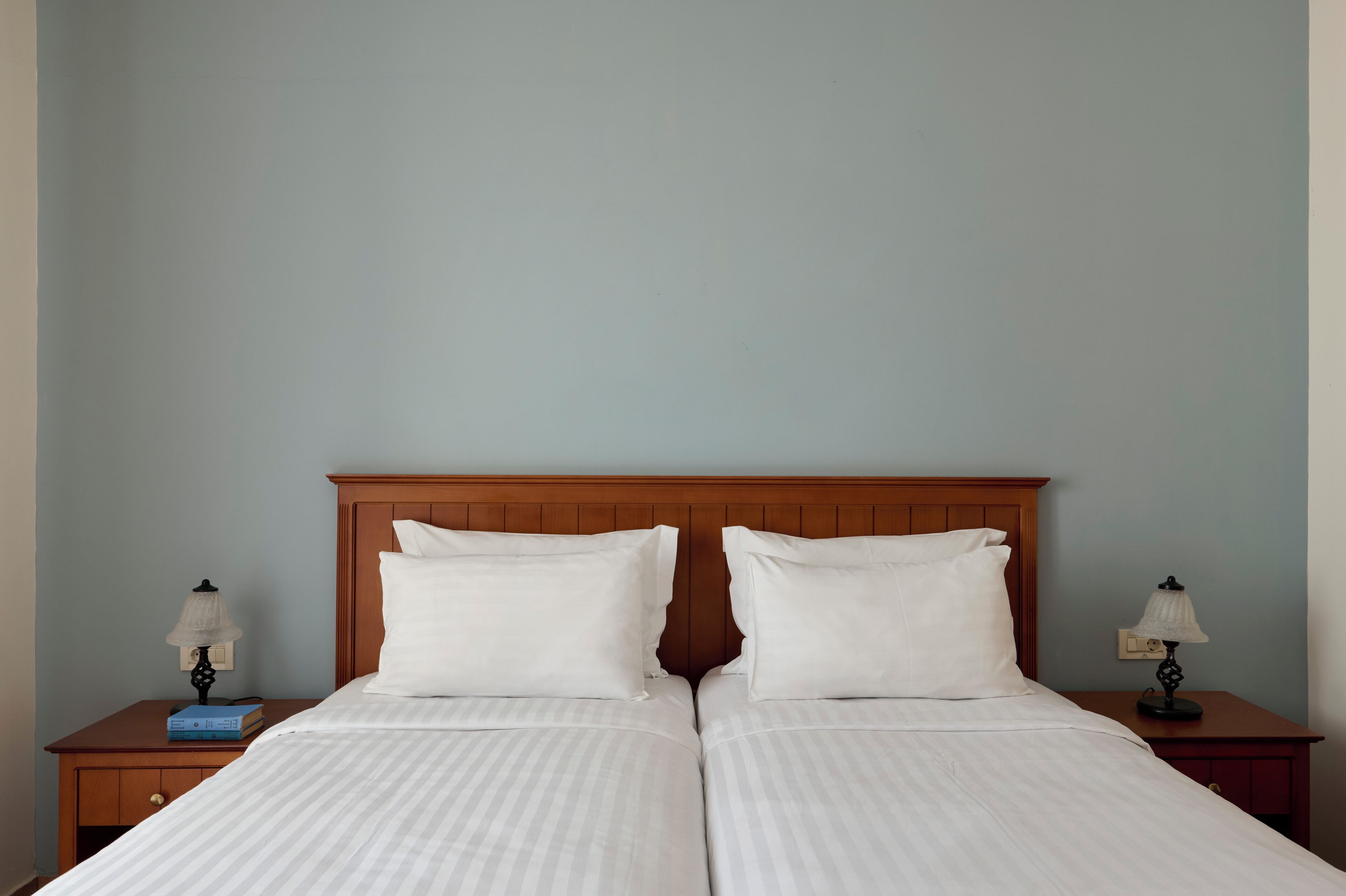 A double bed with a wooden headboard, two bedside tables with lamps, and a light blue wall.