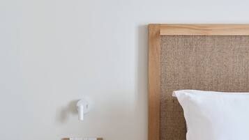 Habitación de hotel impecable con una mesita de noche de madera, un jarrón blanco, un libro y una cama con ropa blanca.