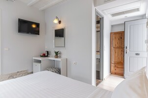 Un dormitorio moderno con una cama, un televisor montado en la pared, un escritorio pequeño con una planta y una puerta de madera.