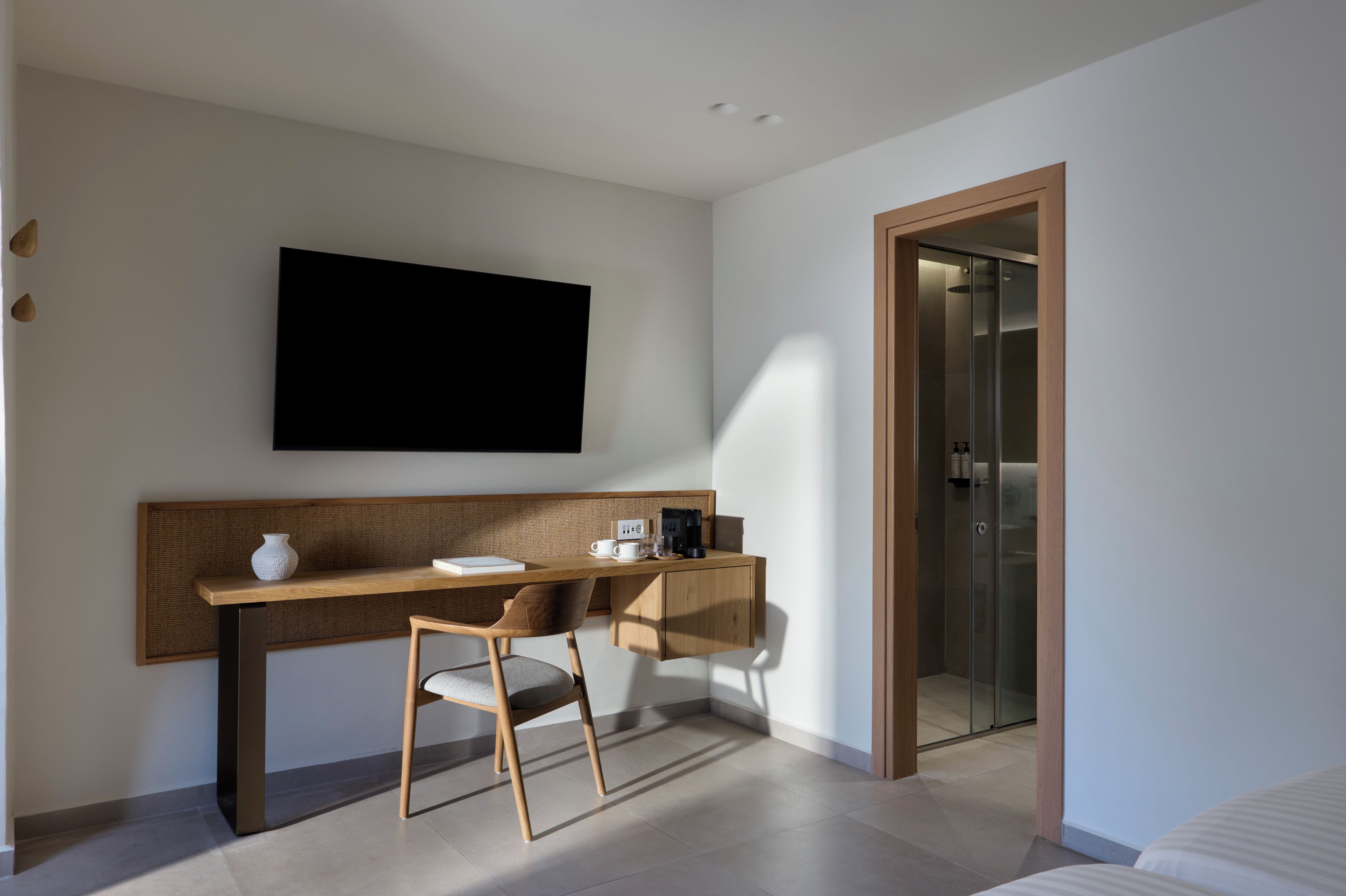 Une chambre d’hôtel moderne, dotée d’un bureau en bois, d’une chaise, d’un téléviseur à écran plat fixé au mur et d’une porte de douche en verre.