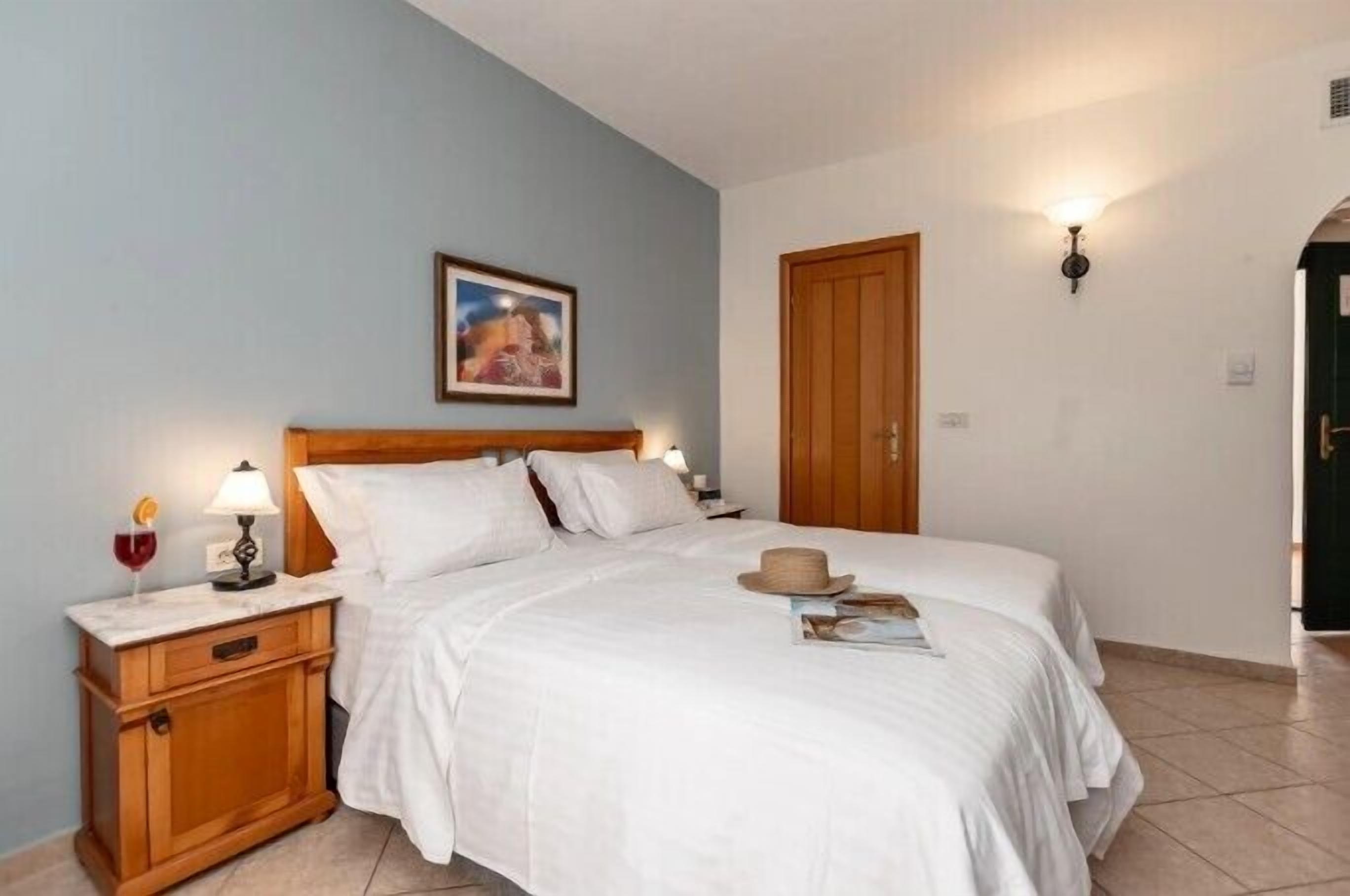 A neatly made bed with white linens, a wooden nightstand with a lamp, and a framed picture on the wall.