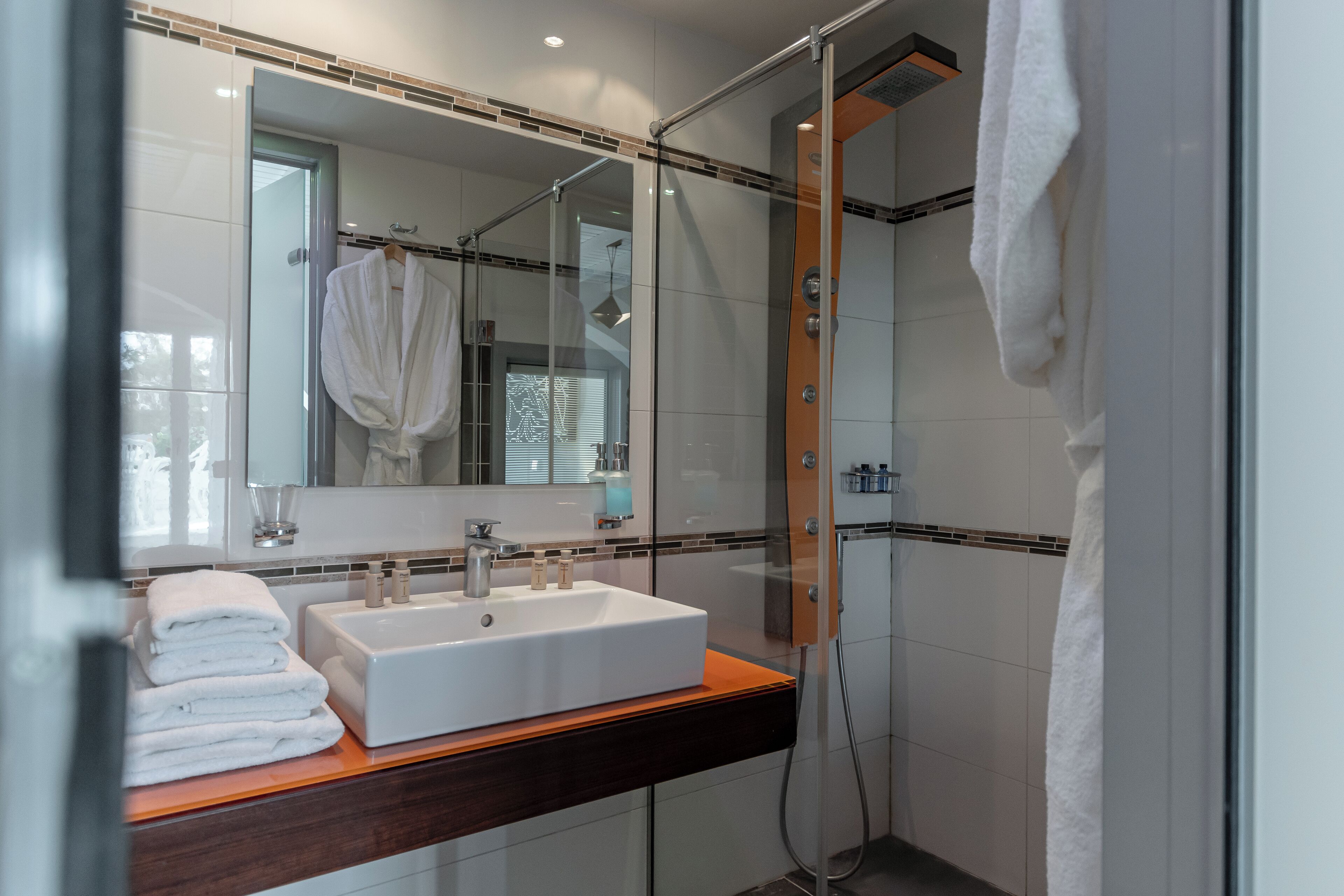 A modern bathroom with a glass-enclosed shower, a wooden vanity with a white sink, and a large mirror.