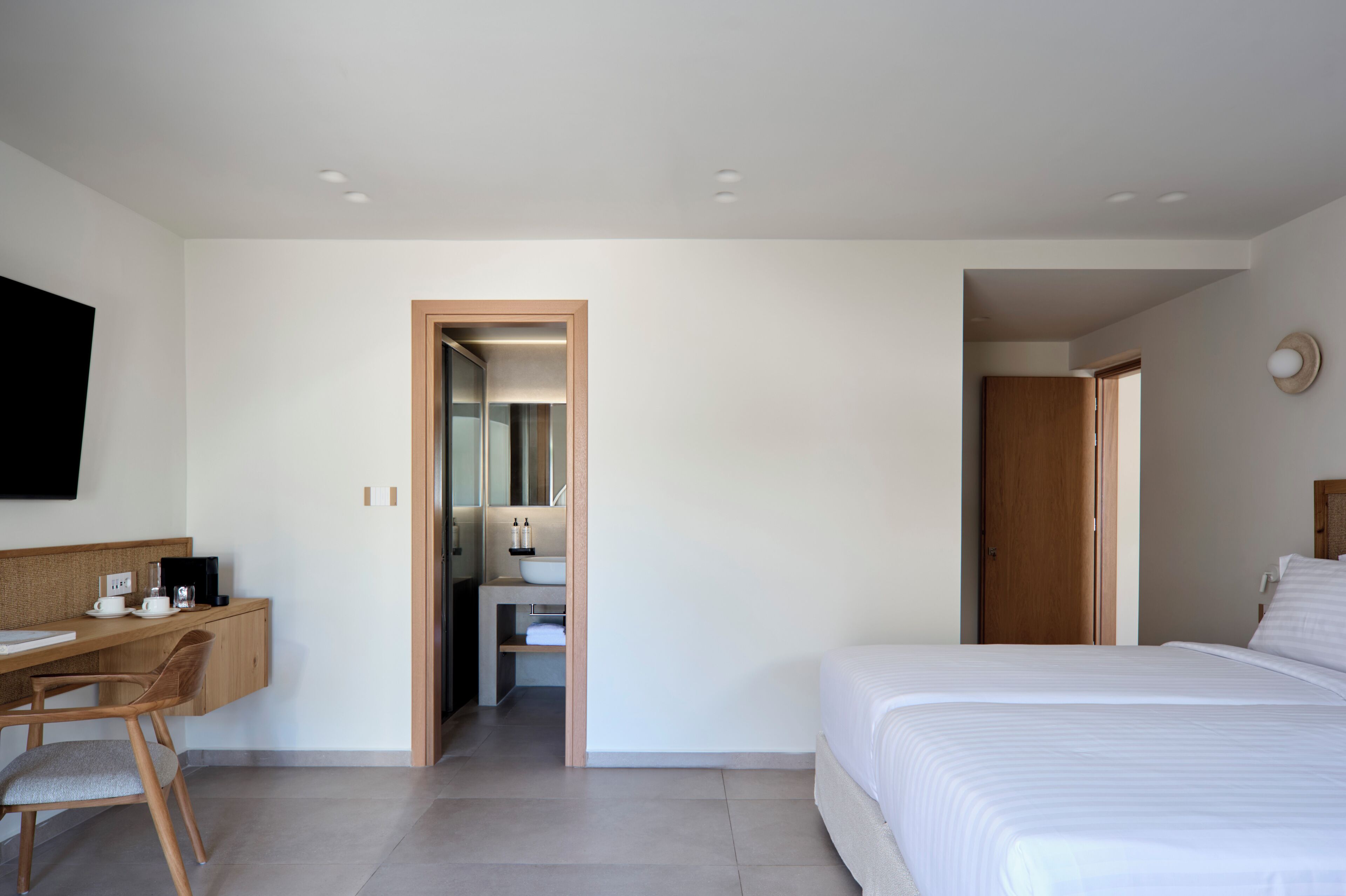 Una habitación de hotel moderna con una cama, un escritorio y un baño visible a través de una puerta abierta.