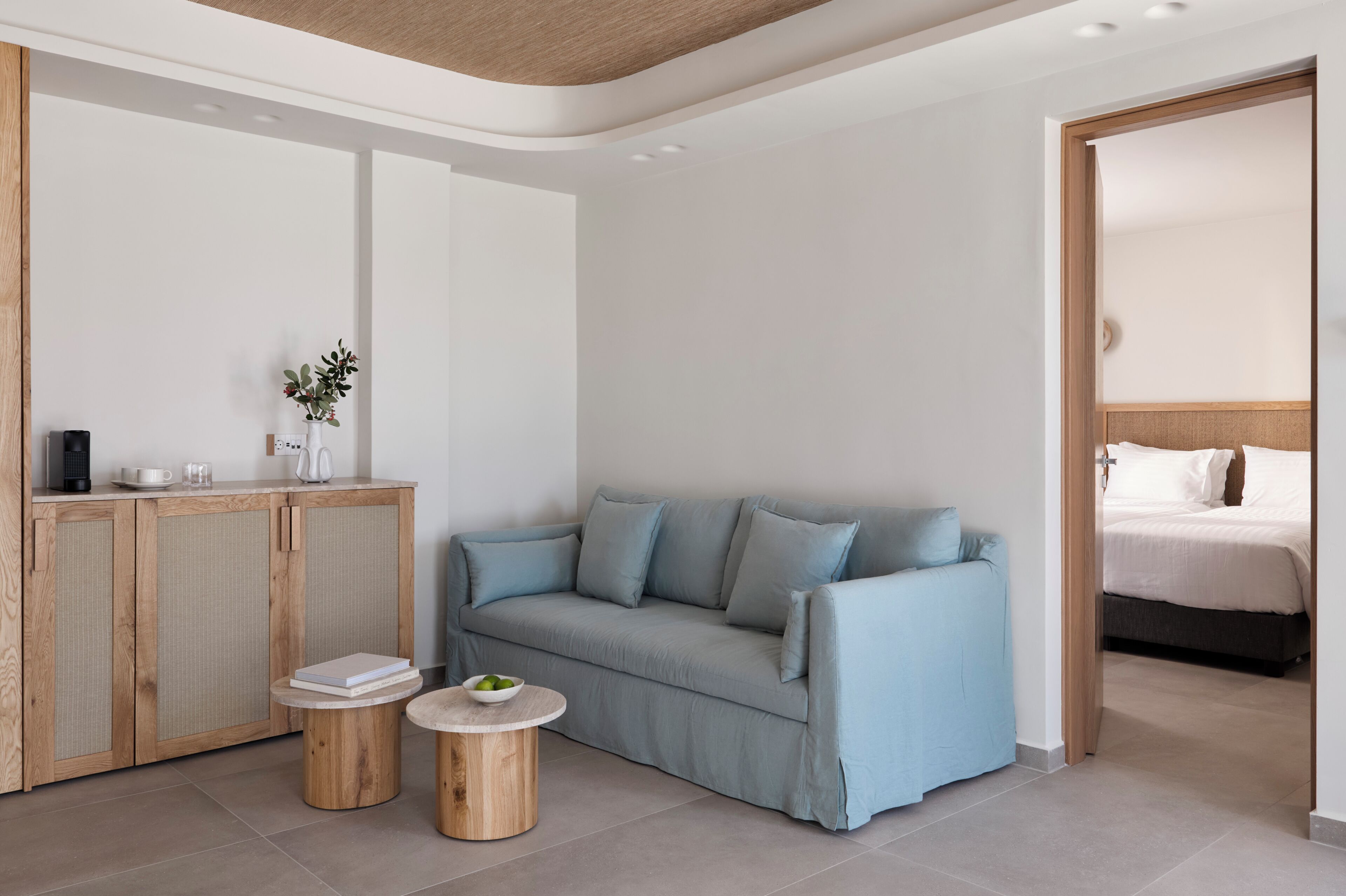 A modern hotel room with a light blue sofa, a wooden cabinet, and a small round table with a bowl of fruit.