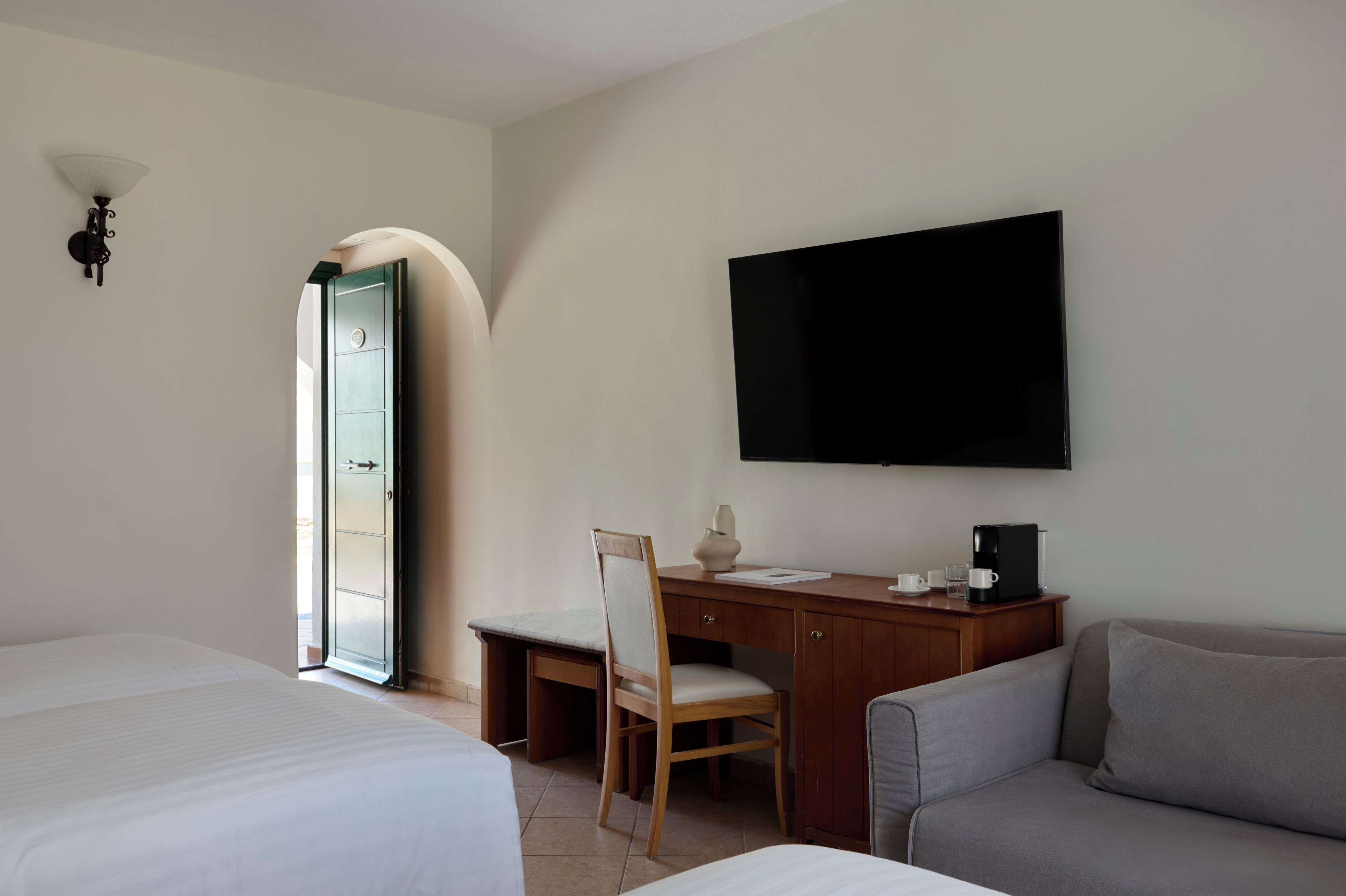 A hotel room with a bed, a desk with a chair, a television, and a sofa.