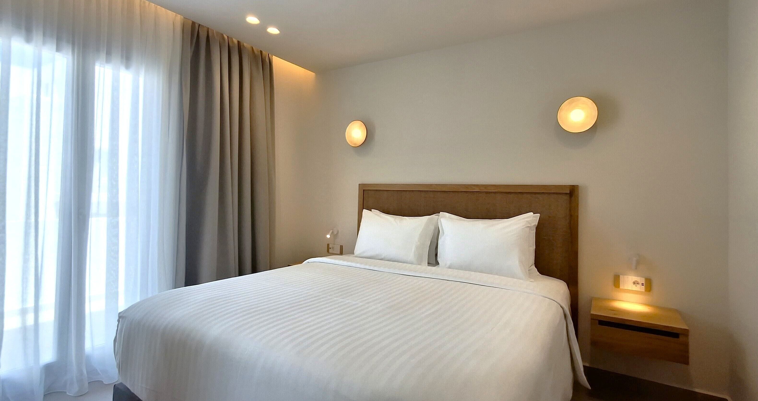 Ein Hotelzimmer mit einem großen Bett, zwei Nachttischlampen, einem Nachttisch und einem Fenster mit Vorhängen.