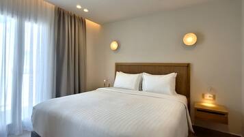 A hotel room with a large bed, two bedside lamps, a nightstand, and a window with curtains.