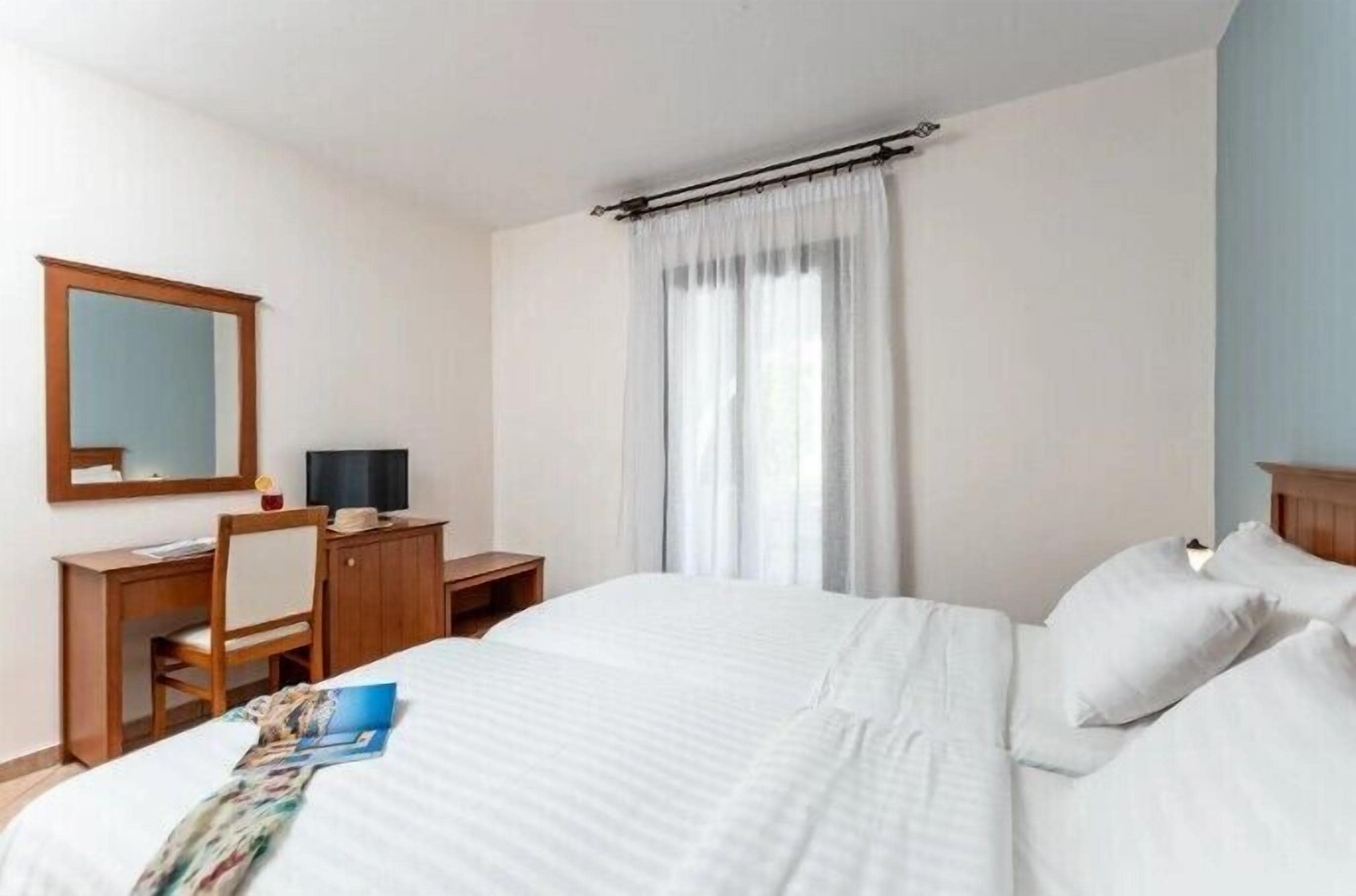 Ein Hotelzimmer mit Bett, Schreibtisch, Stuhl, Spiegel und einem Fenster mit Vorhängen.