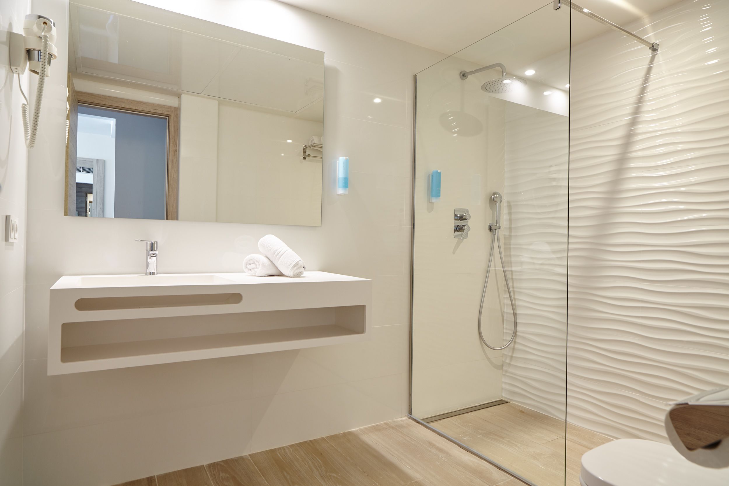 A modern bathroom with a glass shower enclosure, a white vanity with a mirror, and a wooden floor.