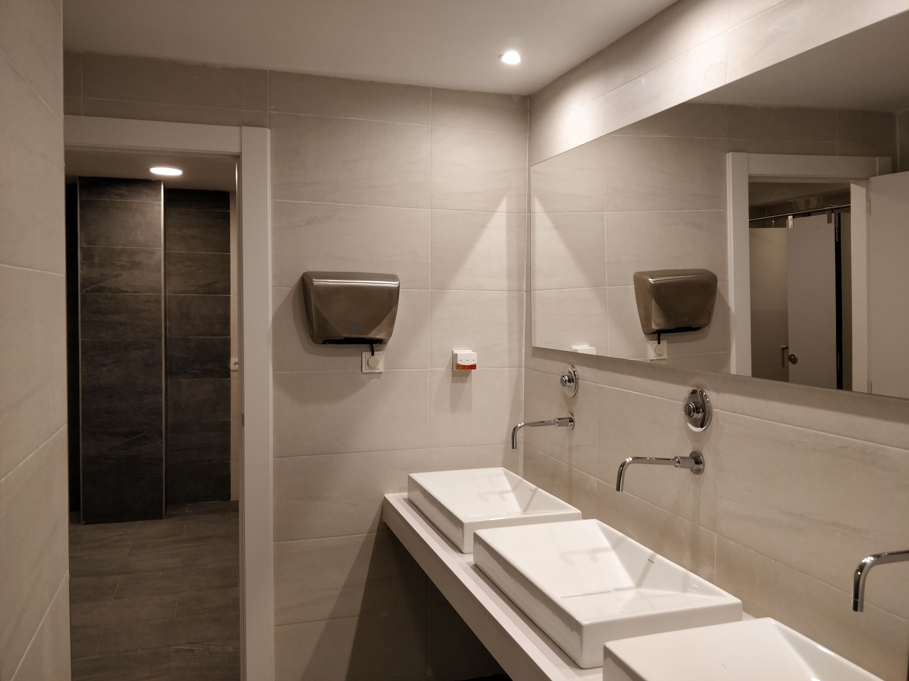 A modern bathroom with three white sinks, a large mirror, and a hand dryer.