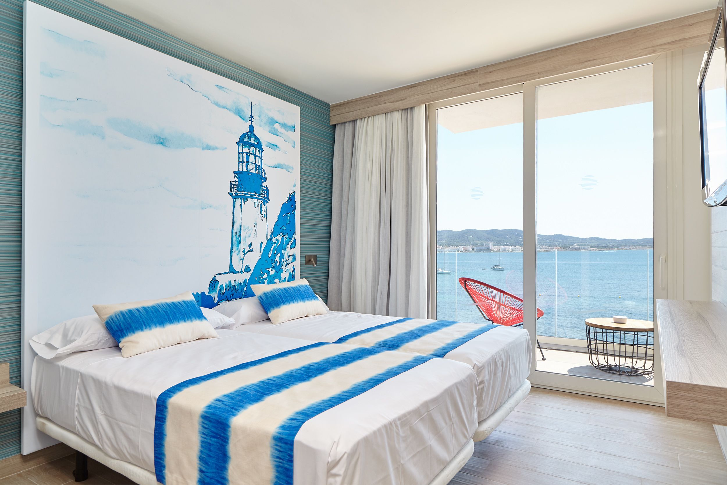 Un dormitorio con una cama grande, vista al mar y una silla roja junto a la ventana.