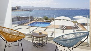 Ein Balkon mit Pool, Liegestühlen und Blick auf das Meer und entfernte Gebäude.