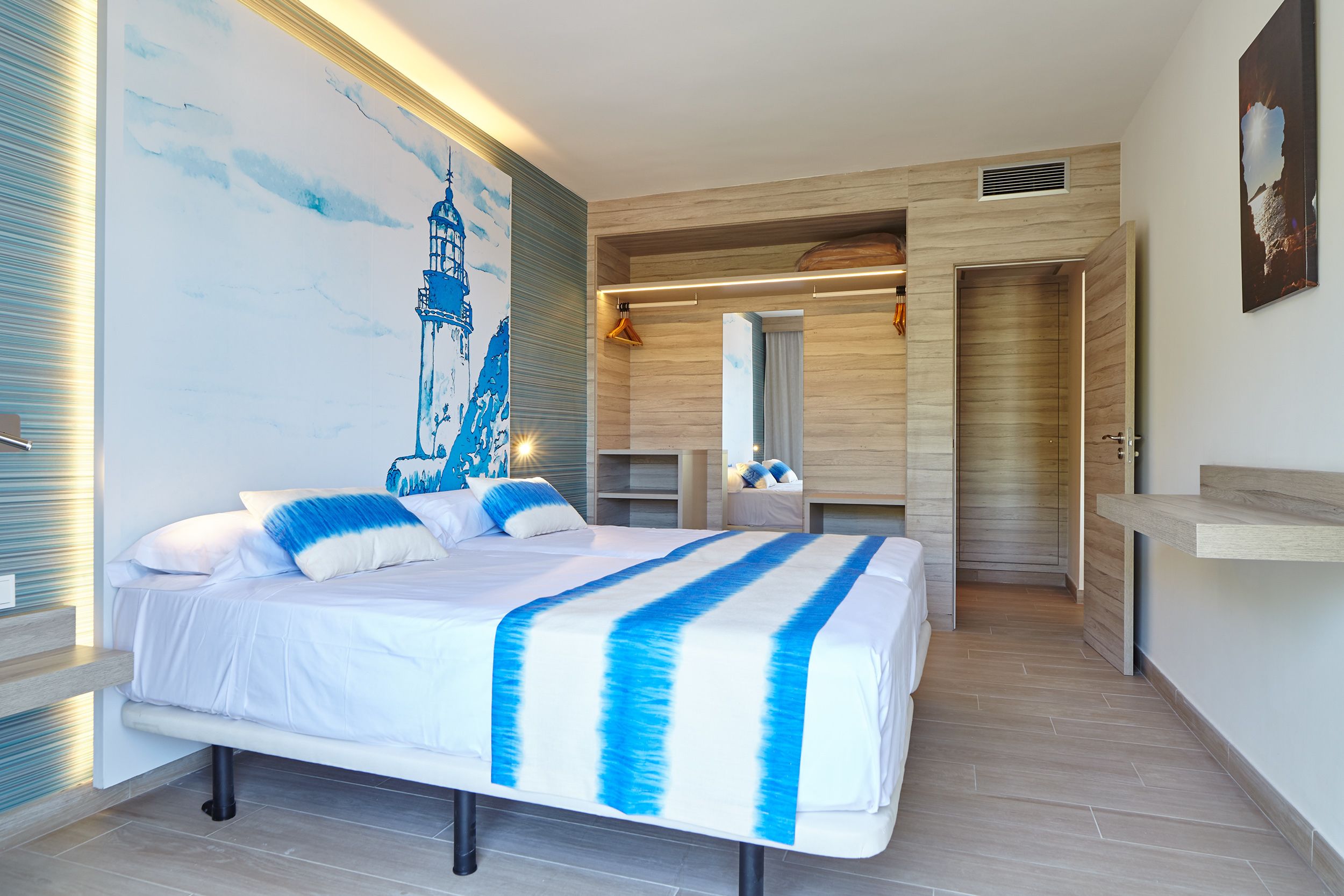A modern bedroom with a large bed, a wooden floor, a painting of a lighthouse, and a built-in wardrobe.
