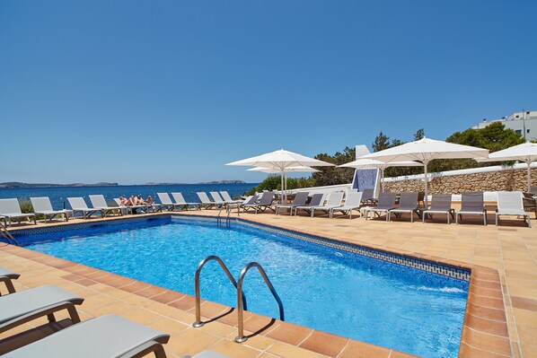 A swimming pool with lounge chairs and umbrellas, overlooking a clear blue sea. - Sol Bahia Ibiza Suites (Sant Antoni de Portmany)
