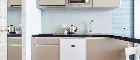 A compact kitchen with a built-in microwave, a kettle, and a small refrigerator.