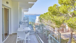 Ein Balkon mit Glastrennwand, weißen Möbeln und Blick auf das Meer.
