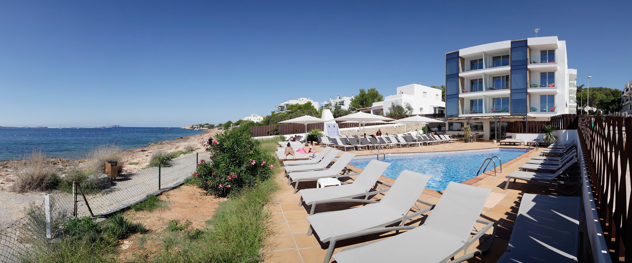A poolside area with lounge chairs, a swimming pool, and a view of the sea.