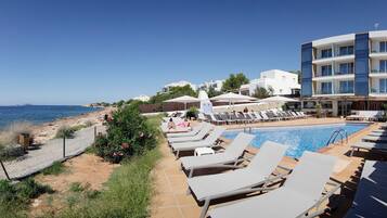 A poolside area with lounge chairs, a swimming pool, and a view of the sea.
