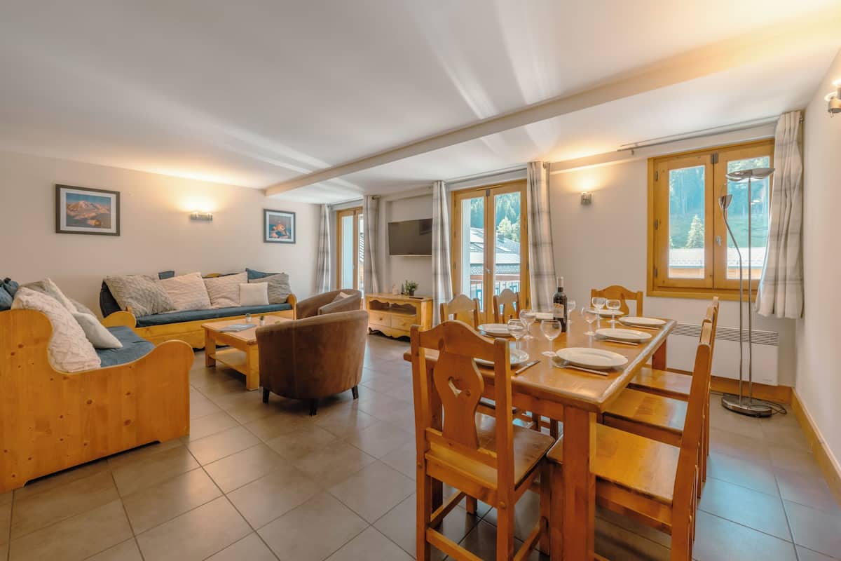 Un vaste espace de vie comprenant un canapé en bois, une table à manger pour quatre personnes et un téléviseur fixé au mur.