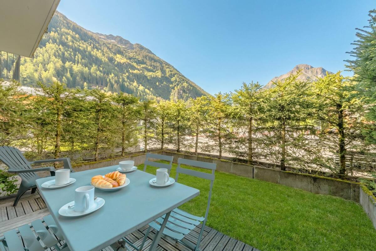 Une table dressée à l’extérieur, avec vue sur la montagne, des chaises et une assiette de croissants.