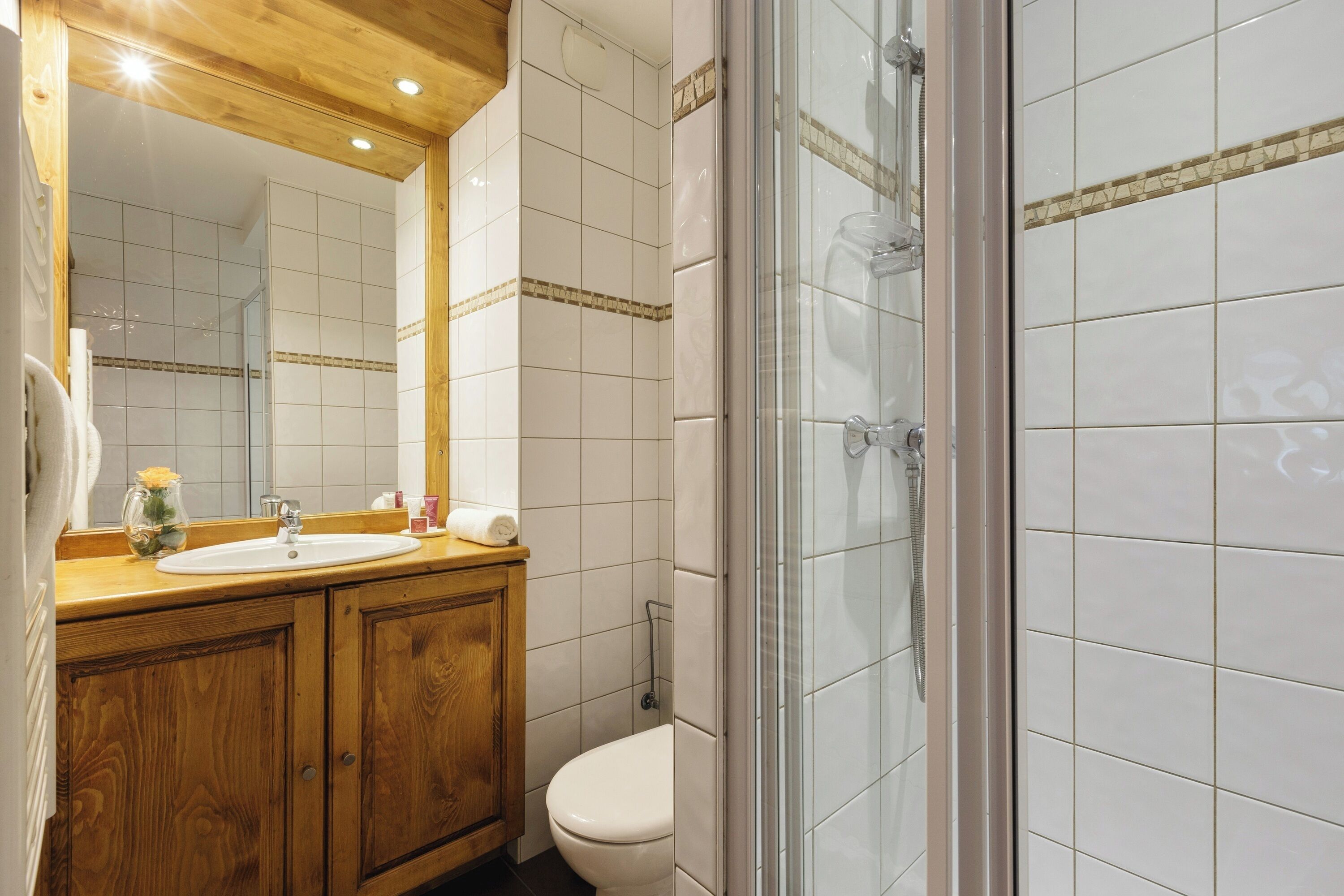 A bathroom with a wooden vanity, a white sink, a toilet, and a glass shower enclosure.