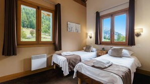 Ein Zimmer mit zwei Betten, einem Heizkörper, einem Fenster mit Vorhängen, einer Wandleuchte und einem Gemälde.