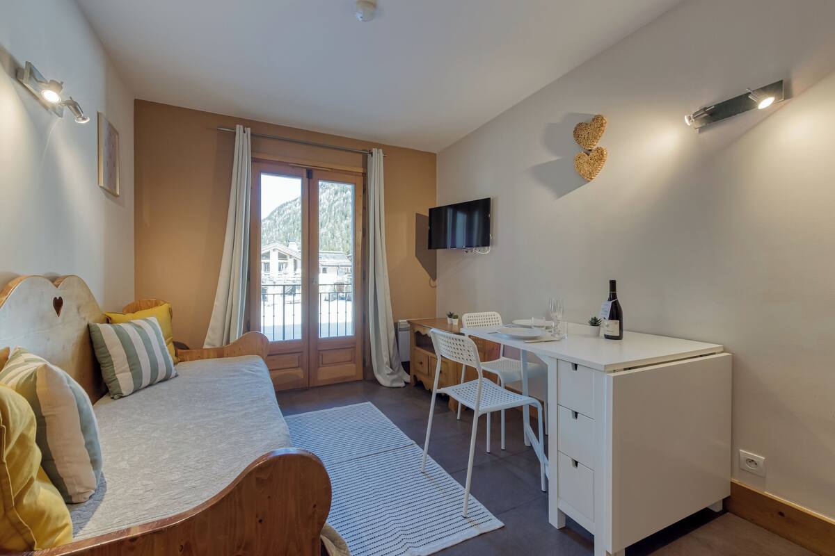 Une chambre à coucher avec un lit, un bureau, une chaise, un téléviseur et une fenêtre avec des rideaux.