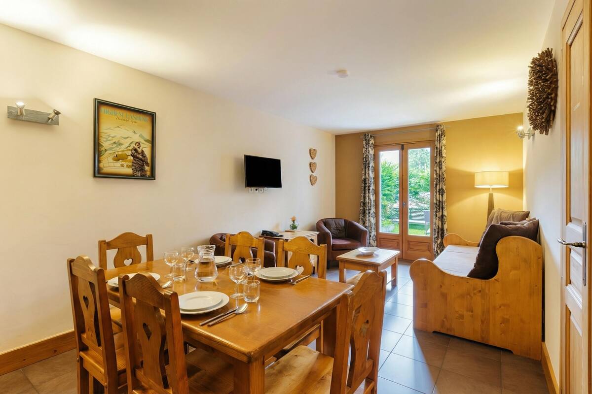 Un coin repas avec une table et des chaises en bois, un téléviseur fixé au mur et une fenêtre avec des rideaux.