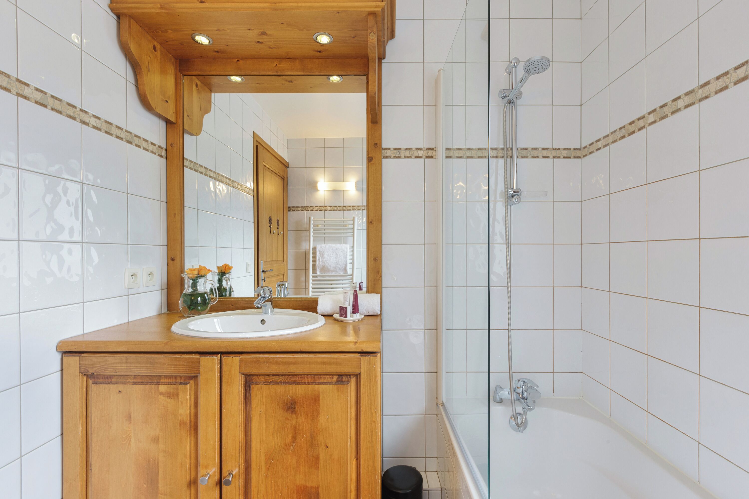 Een badkamer met een houten wastafelmeubel, een wastafel, een spiegel en een douche met glazen wanden.