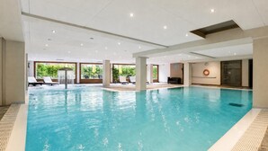 Ein großes Hallenbad mit klarem Wasser, umgeben von Liegestühlen und einer Decke mit eingelassener Beleuchtung.