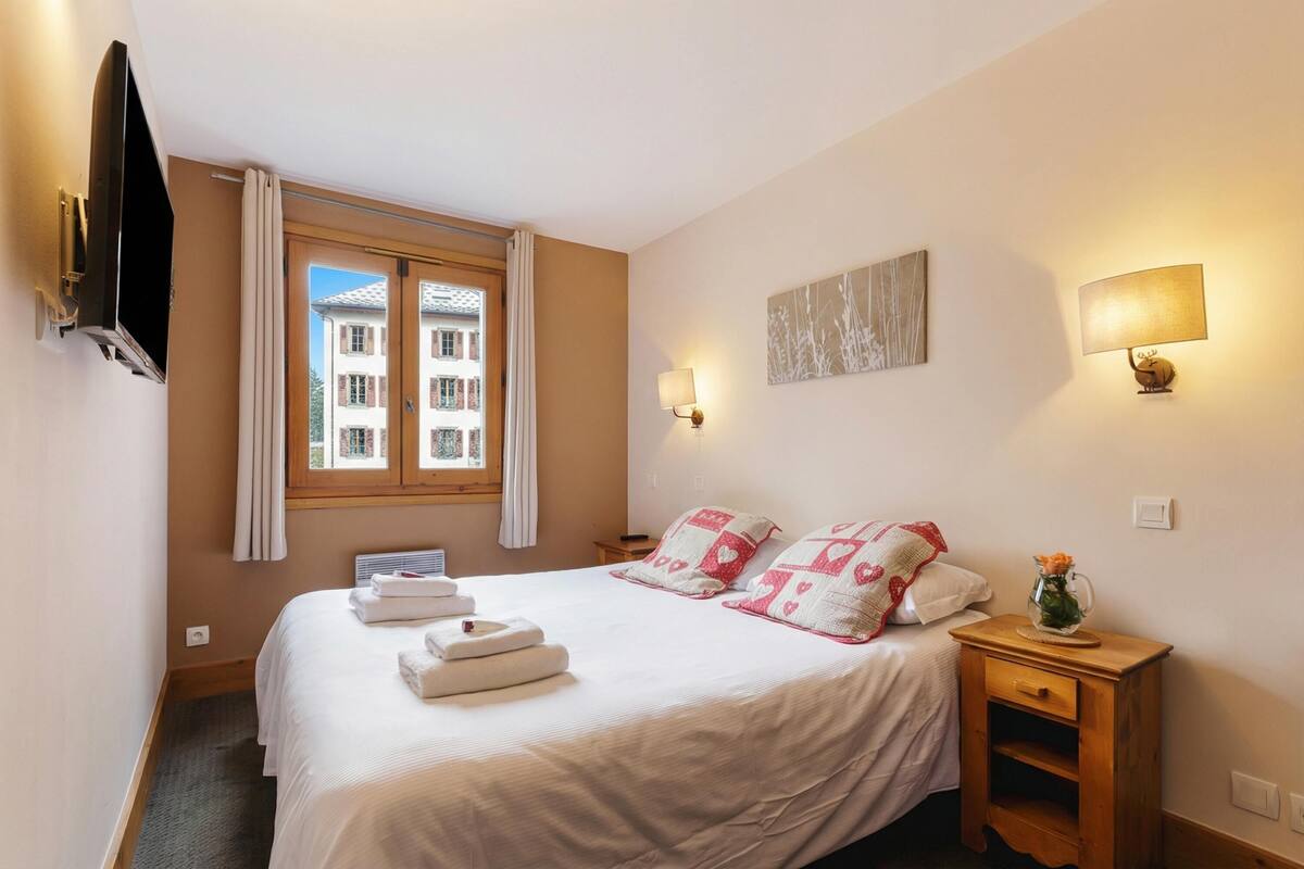 Une chambre d’hôtel comprenant un lit, une télévision, une fenêtre avec des rideaux, une lampe de chevet et une œuvre d’art accrochée au mur.