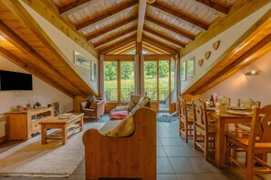 A cozy attic room with wooden beams, a large window, a sofa, a dining table set for four, and a TV on the wall. - Vallorcine Apartments (Vallorcine)