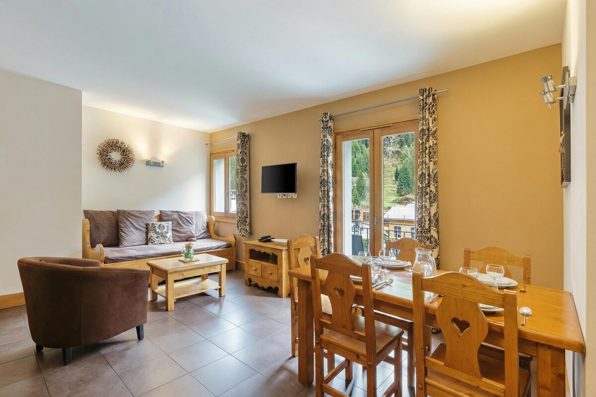 A modern living room with a sofa, a wooden dining table set for four, and a TV mounted on the wall.
