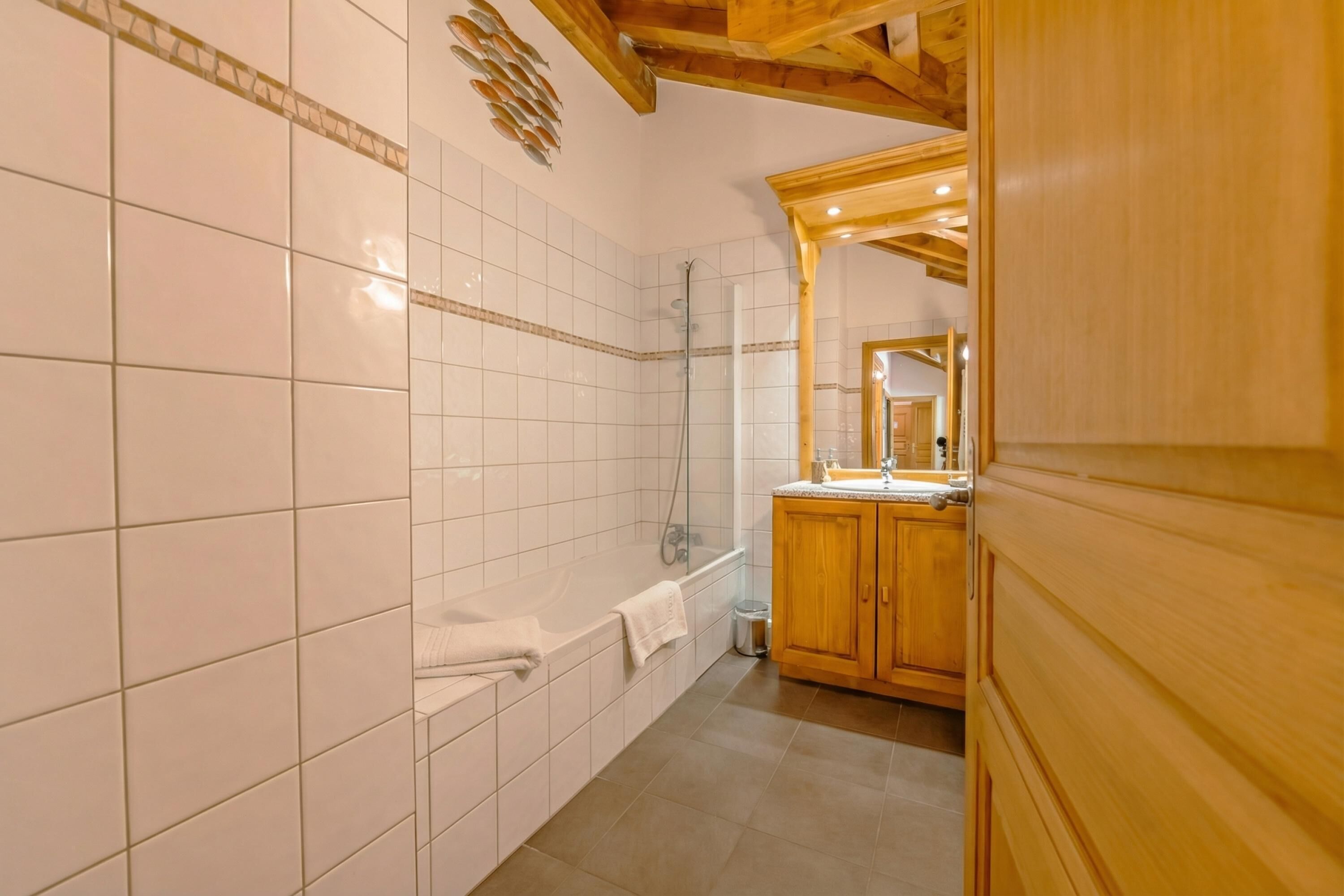 A bathroom with white tiled walls, a wooden vanity, a bathtub, and a shower.