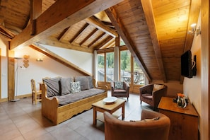 A cozy loft-style room with a wooden ceiling, a sofa, a chair, a small table, and a TV mounted on the wall. - Vallorcine Apartments (Vallorcine)