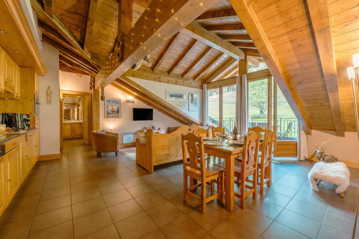 Un intérieur rustique en bois, comprenant un coin repas, une cuisine et offrant une vue sur l’extérieur.
