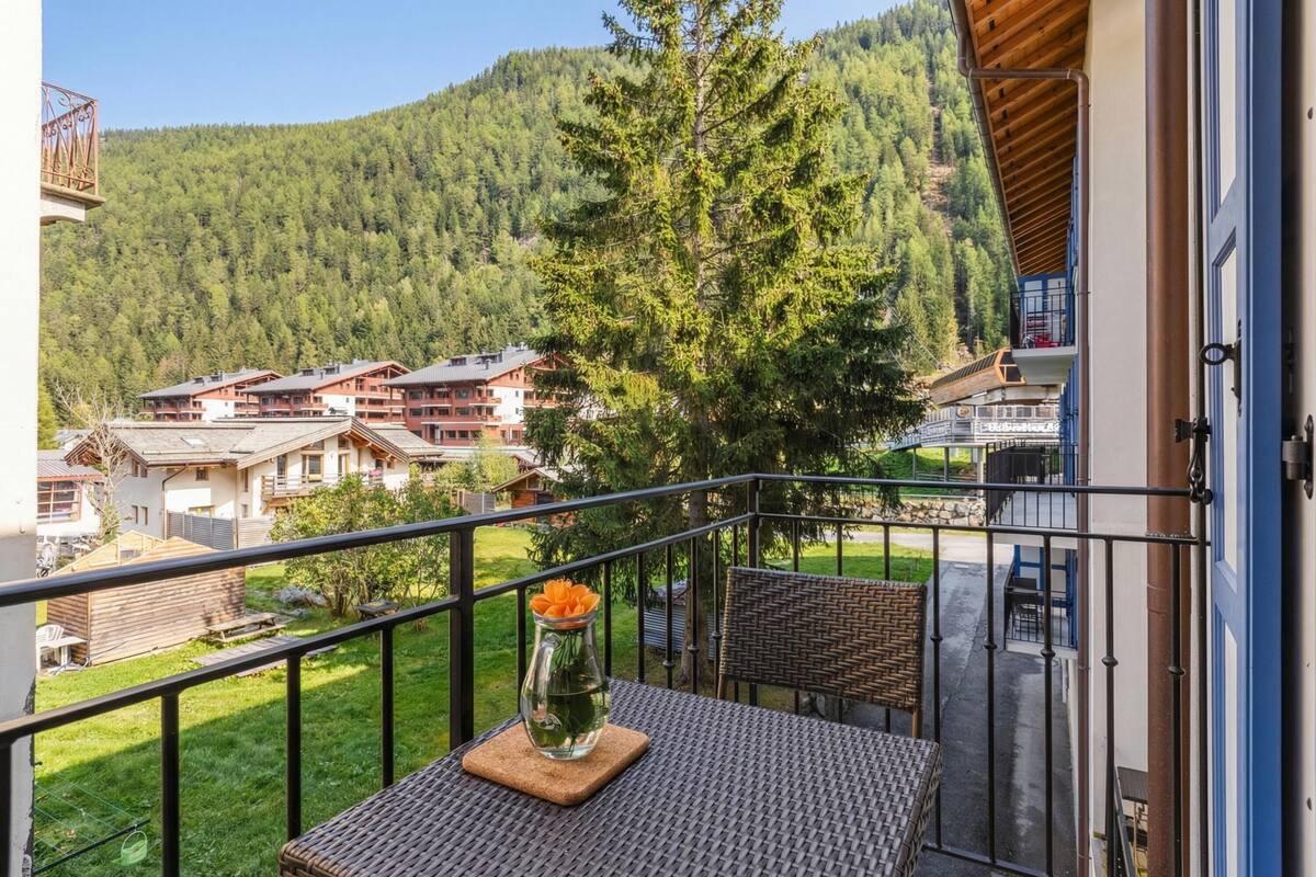 Un balcon avec une table, un vase rempli de fleurs et une vue sur une montagne et des bâtiments.