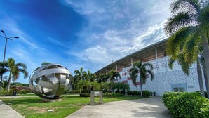 A modern building with a large metallic sculpture in the foreground, surrounded by palm trees and a clear blue sky. - The Beach House (Panama City)