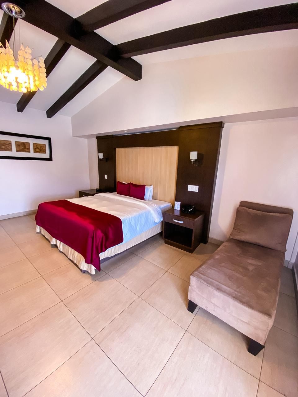Un dormitorio con cama, mesitas de noche, sillón y lámpara de araña.