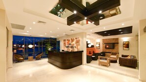 A modern hotel lobby with a reception desk, seating area, and a large window overlooking the city. - The Beach House (Panama City)