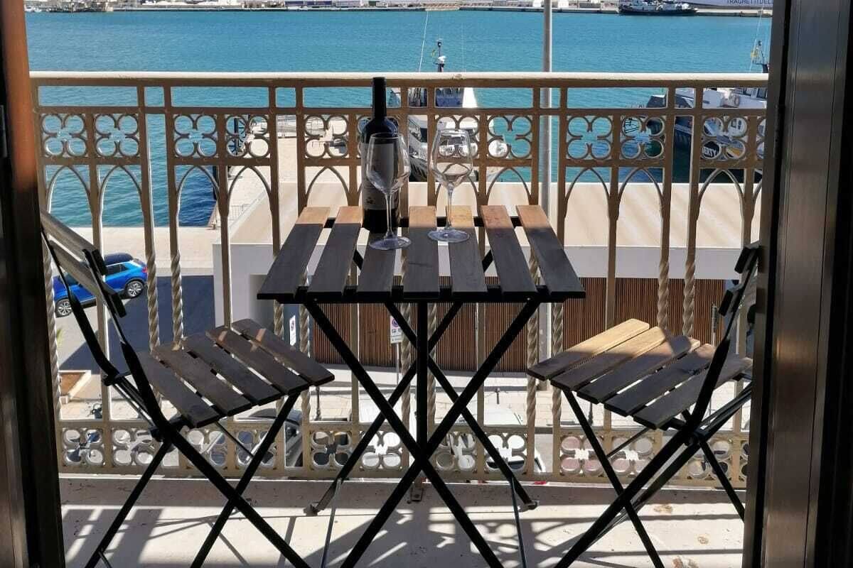 A balcony with a view of the sea, a table with chairs, and a railing.