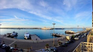 A marina with boats docked, a road with cars, and a building with balconies overlooking the water. - B&b Belveliero (Trapani)