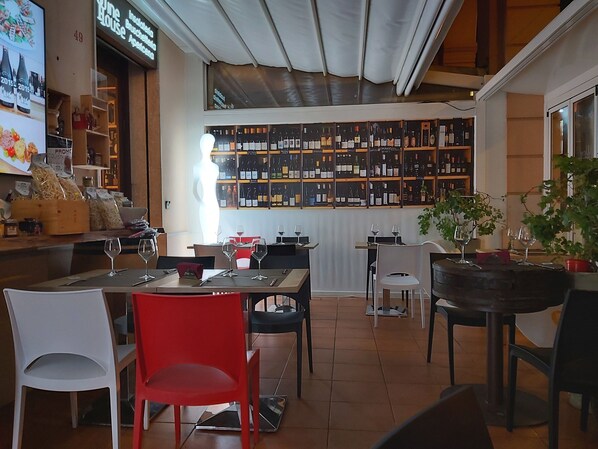 A restaurant interior with a wine wall, tables with chairs, and a counter with food items. - B&b Belveliero (Trapani)